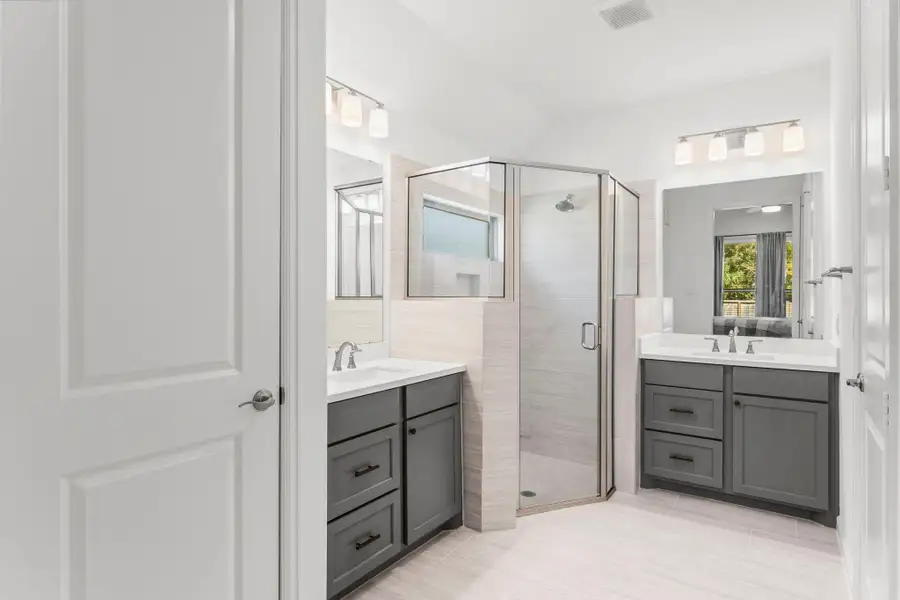 Experience luxury in the primary bath with dual vanities, a sleek corner shower, and ample storage in both the linen and walk-in closets.