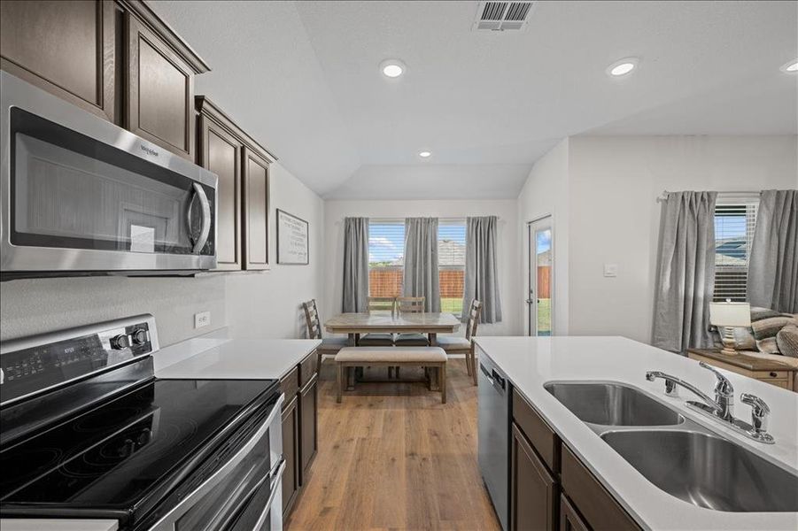 Kitchen with dark brown cabinetry, stainless steel appliances, light wood finished floors, vaulted ceiling, and recessed lighting Kitchen with dark brown cabinetry, stainless steel appliances, light wood finished floors, vaulted ceiling, and recessed lighting