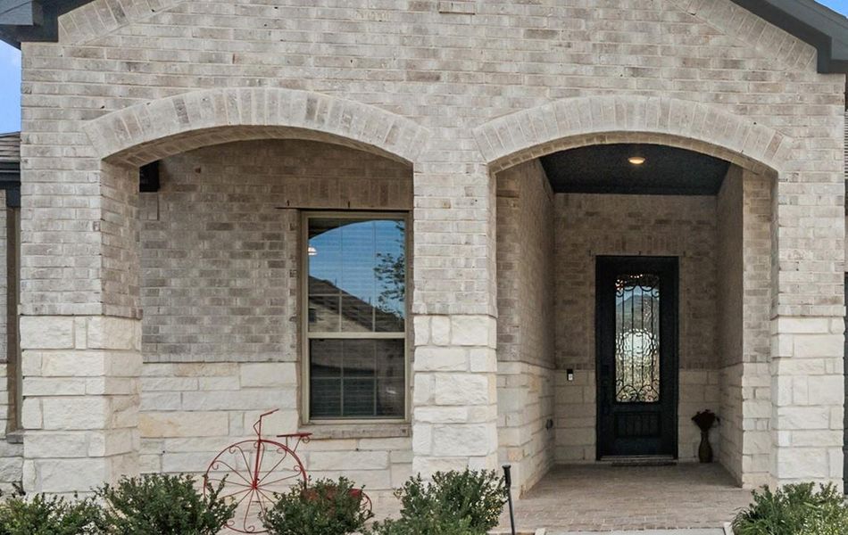 The upgrades in this home include a bricked front porch. Note the modern ironwork wood door.