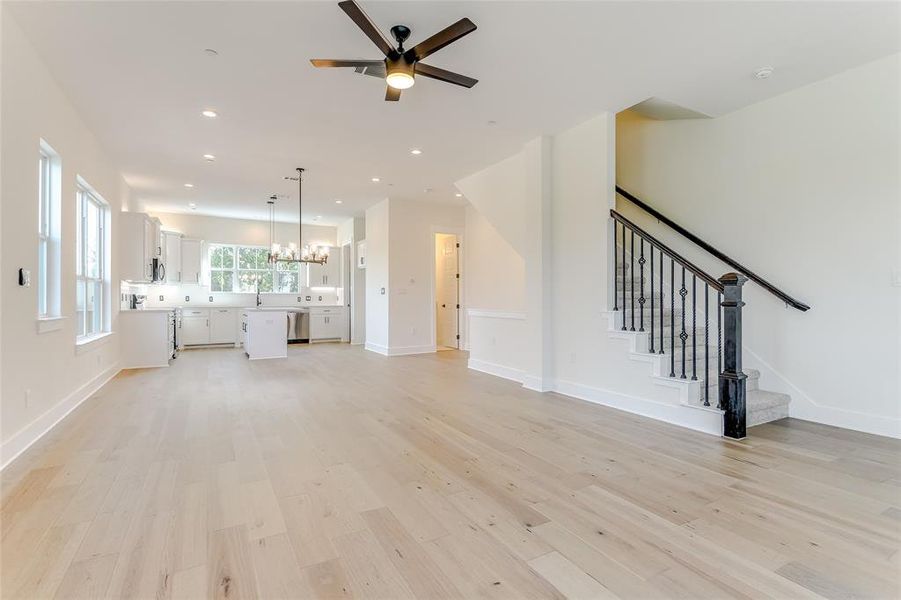 Unfurnished living room featuring sink, light hardwood / wood-style floors, and ceiling fan with notable chandelier