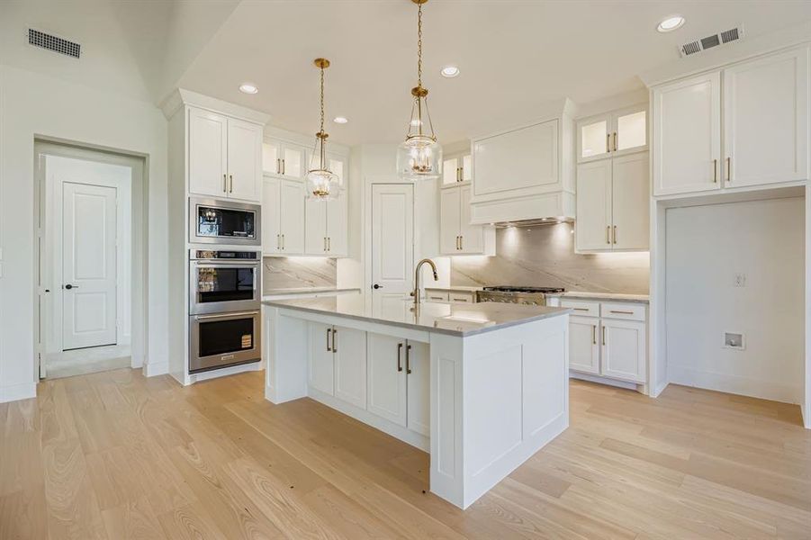 Kitchen with appliances with stainless steel finishes, decorative light fixtures, glass insert cabinets, white cabinets, and recessed lighting Kitchen with appliances with stainless steel finishes, decorative light fixtures, glass insert cabinets, white cabinets, and recessed lighting