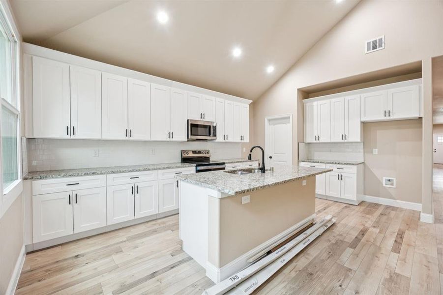 Kitchen featuring decorative backsplash, light stone counters, stainless steel appliances, white cabinets, and high vaulted ceiling Kitchen featuring decorative backsplash, light stone counters, stainless steel appliances, white cabinets, and high vaulted ceiling