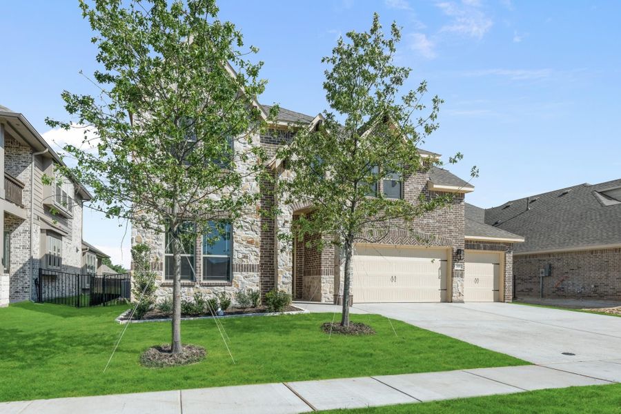 Two-story home with stone and brick exterior, two-car garage, and green front lawn with young trees