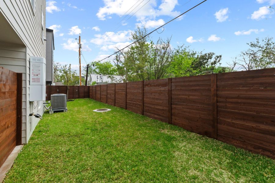 A tall wooden fence encloses the grassy side yard beneath a clear blue sky.