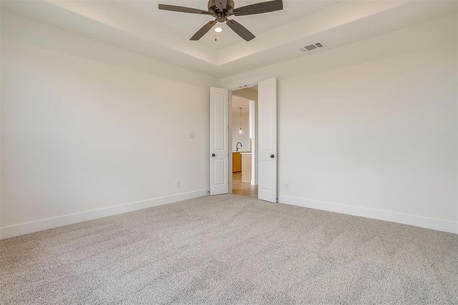 Carpeted empty room featuring a tray ceiling and ceiling fan