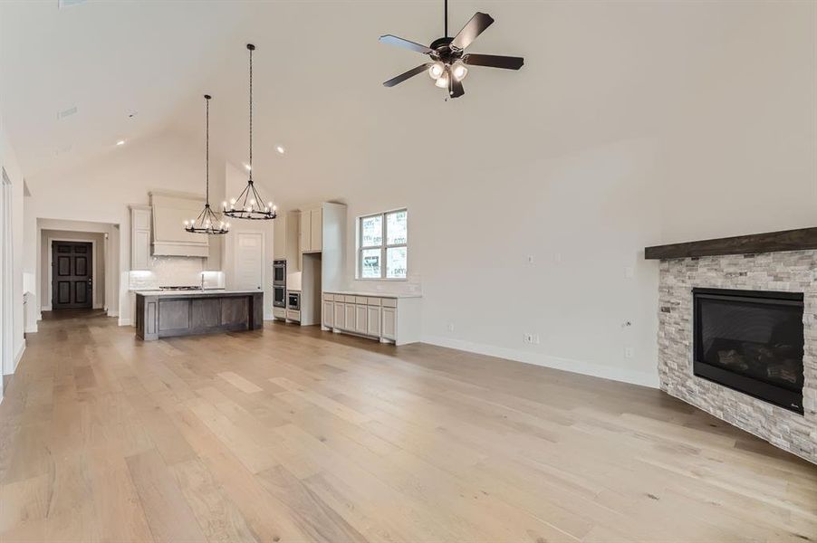 Unfurnished living room featuring light hardwood / wood-style floors, ceiling fan with notable chandelier, a fireplace, and high vaulted ceiling