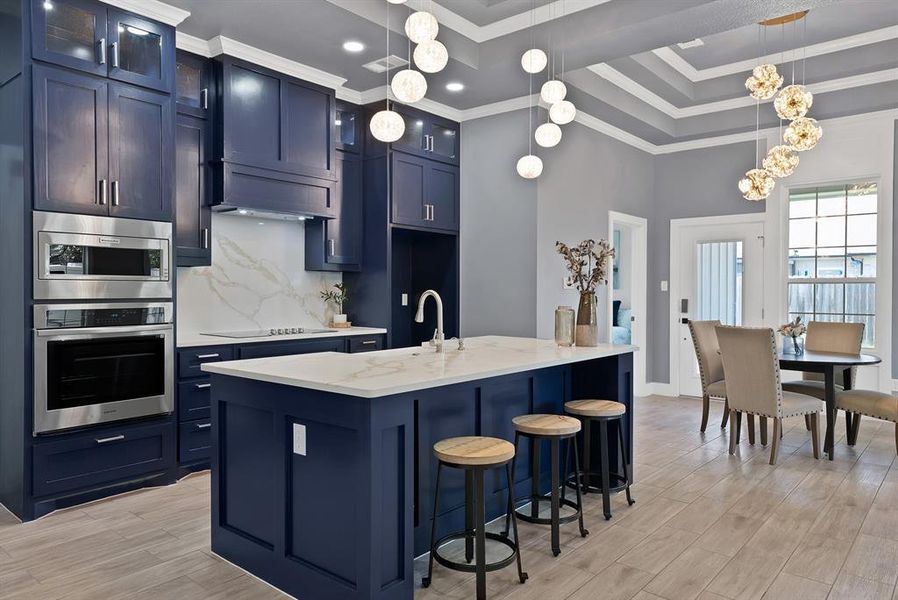 Gourmet kitchen featuring navy cabinetry, stainless steel appliances, a large central island with seating, and a marble-patterned backsplash
