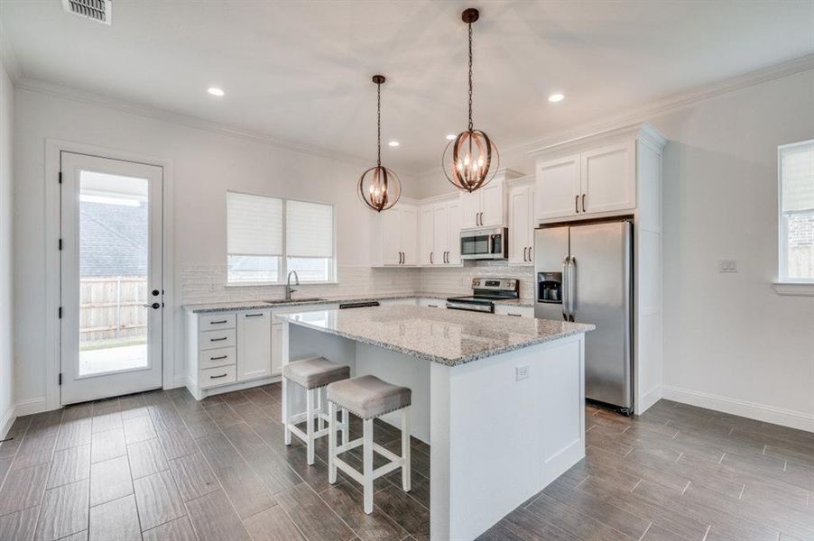 Kitchen featuring stainless steel appliances, sink, decorative light fixtures, a center island, and white cabinetry