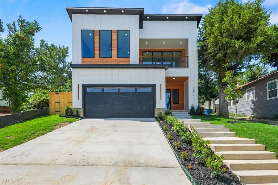 Modern home with a balcony, concrete driveway, a garage, stairway, and board and batten siding