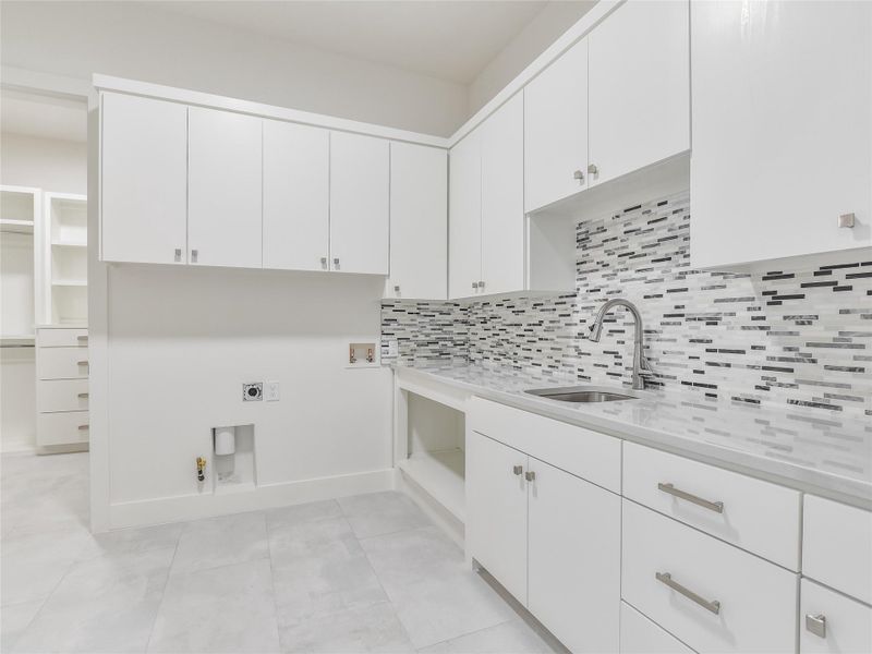 Laundry room with light tile patterned floors, a sink, white cabinets, light countertops, and backsplash