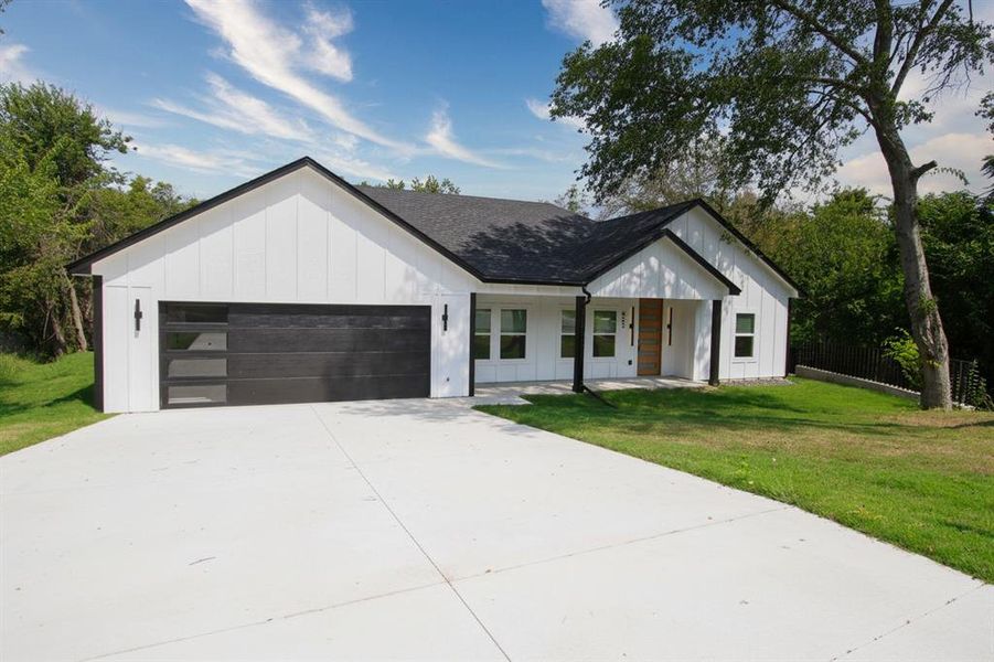 Modern inspired farmhouse featuring board and batten siding, concrete driveway, covered porch, a garage, and roof with shingles Modern inspired farmhouse featuring board and batten siding, concrete driveway, covered porch, a garage, and roof with shingles