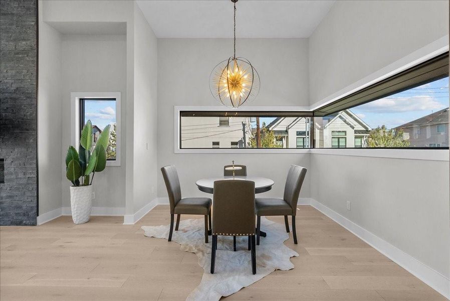 This dining area features a modern chandelier, a round table with four chairs, and light wood flooring. Large corner windows provide ample natural light, while a potted plant adds a touch of greenery. This dining area features a modern chandelier, a round table with four chairs, and light wood flooring. Large corner windows provide ample natural light, while a potted plant adds a touch of greenery.