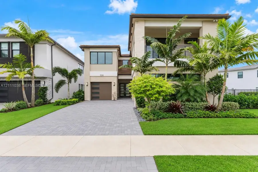 Two-story exterior featuring a paver driveway, second-floor covered balcony with metal railing, multi-panel garage door, and contemporary architectural design
