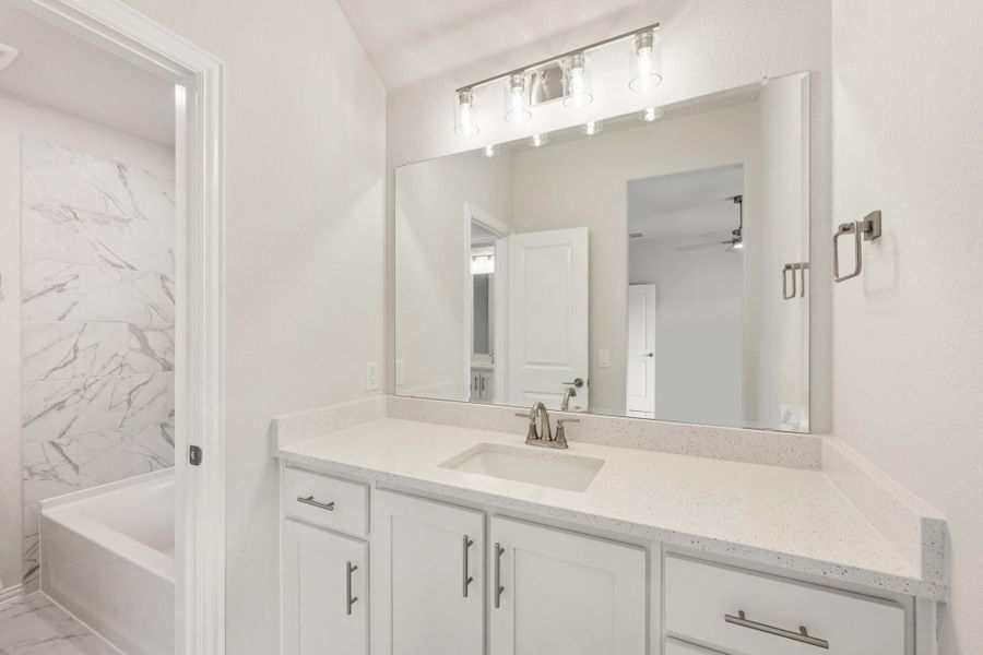 Bathroom with white vanity, quartz countertop, large mirror, and marble-tiled soaking tub surround