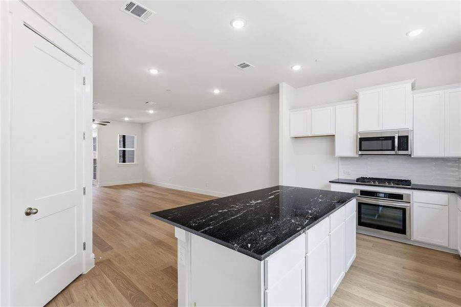 Kitchen featuring a dark granite island, white cabinetry, stainless steel appliances, and light wood flooring