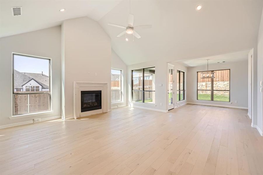 Unfurnished living room featuring ceiling fan with notable chandelier, high vaulted ceiling, and light hardwood / wood-style floors