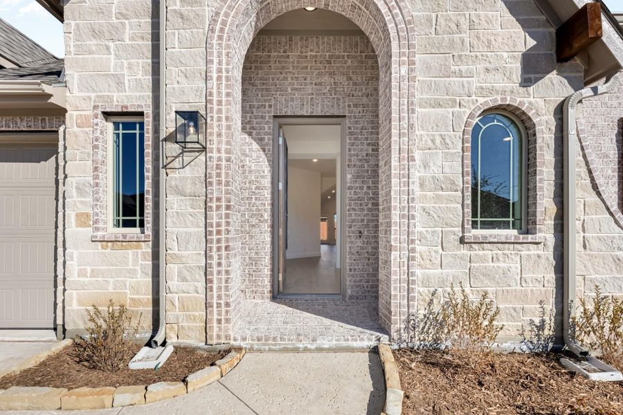 Home entrance with arched brick doorway, stone exterior, and wall-mounted lantern light fixture Home entrance with arched brick doorway, stone exterior, and wall-mounted lantern light fixture
