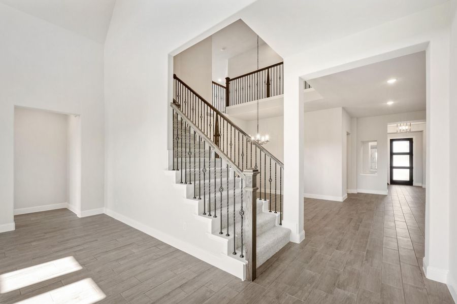 Foyer with carpeted staircase, iron balusters, high ceilings, and wood-look tile floors leading to front entry door. Foyer with carpeted staircase, iron balusters, high ceilings, and wood-look tile floors leading to front entry door.