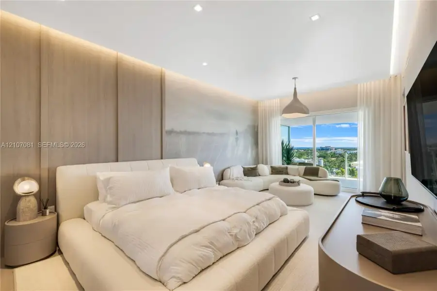 Wood-finish paneled accent wall, recessed lighting, integrated cove lighting, and floor-to-ceiling glass sliding doors opening to a balcony Wood-finish paneled accent wall, recessed lighting, integrated cove lighting, and floor-to-ceiling glass sliding doors opening to a balcony