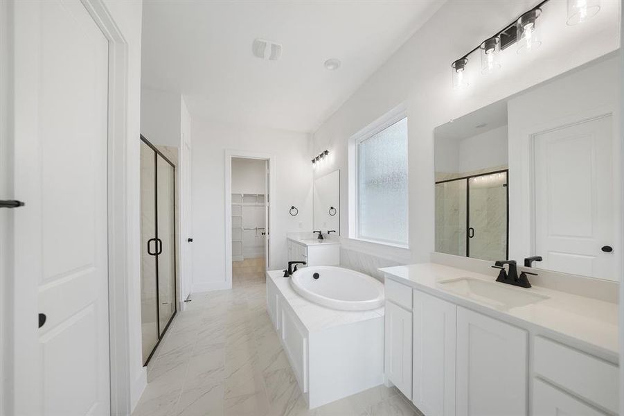 Full bathroom featuring two vanities, a garden tub, a walk in closet, a marble finish shower, and light marble finish flooring