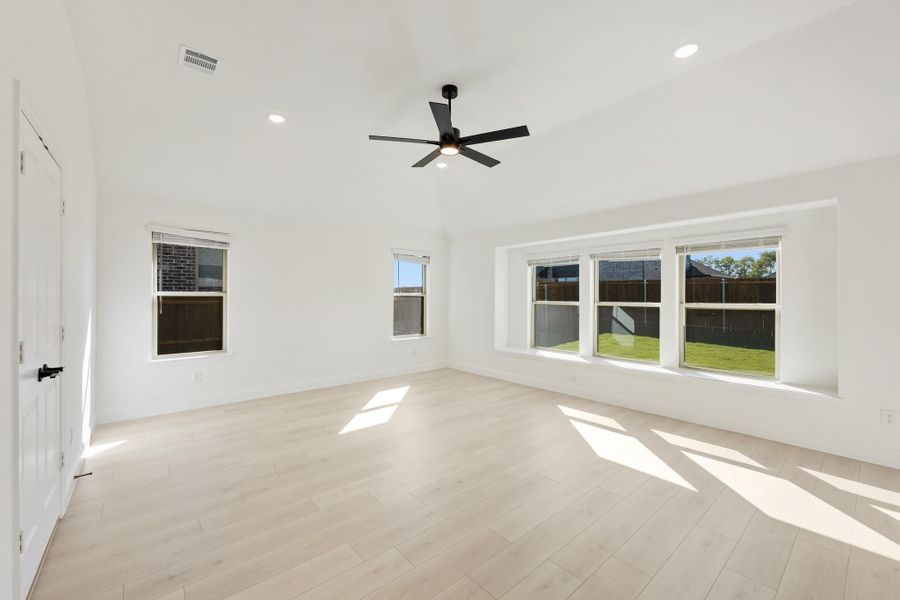 Empty room with light wood floors, white walls, ceiling fan, and large windows overlooking backyard Empty room with light wood floors, white walls, ceiling fan, and large windows overlooking backyard