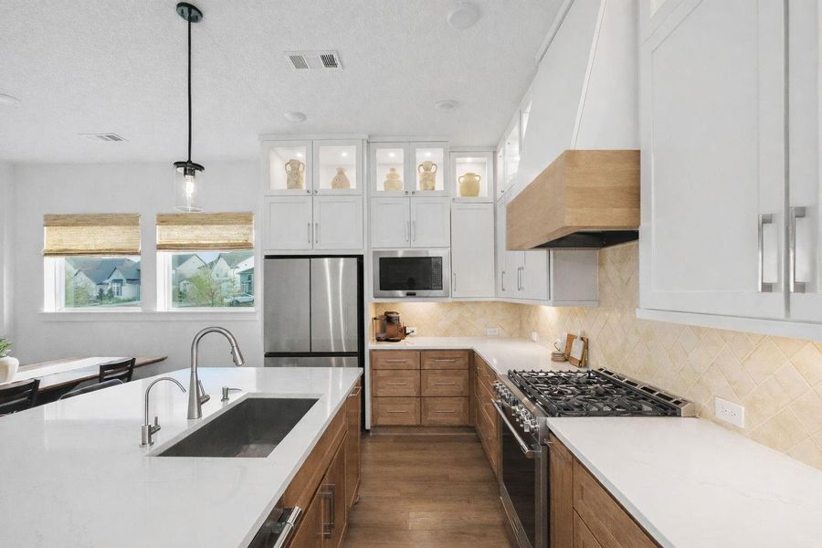 Well-appointed kitchen featuring a spacious prep island with undermount sink, stainless appliances, and generous cabinetry for storage. Lighted upper display cabinets and a warm tile backsplash add depth and style, creating a functional and beautifully finished workspace.