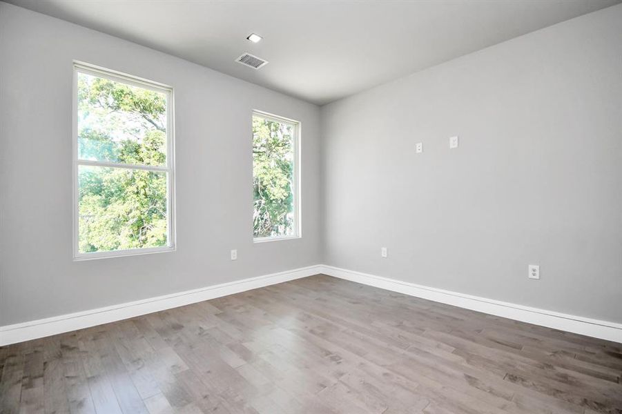 This is a modern, empty room featuring light grey walls, laminate flooring, recessed lighting, and white trim and two large windows that offer a view of greenery outside. It features contemporary wood flooring and recessed lighting.