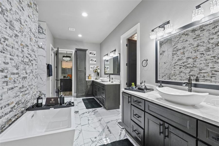 Full bath with two vanities, a freestanding tub, light marble finish flooring, and recessed lighting