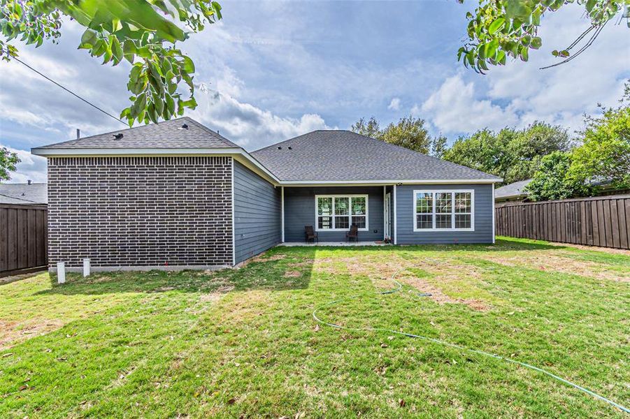 Rear view of property featuring a fenced backyard, a patio area, roof with shingles, and brick siding