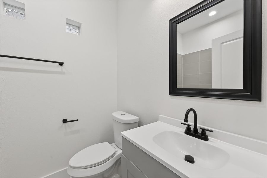 This is a modern bathroom featuring a sleek white vanity with a black framed mirror and matching black fixtures. The space is bright and minimalistic, with a small window providing natural light.