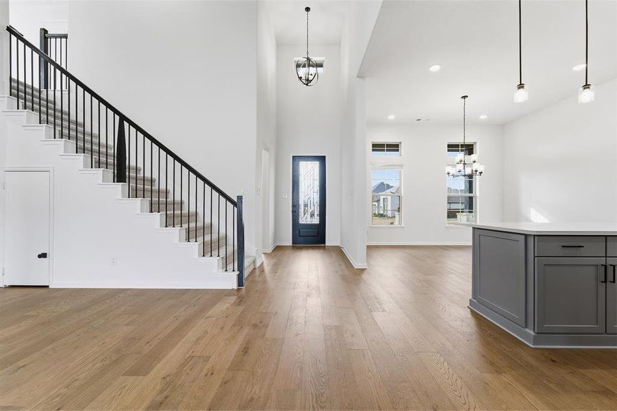 Grand entryway featuring a two-story foyer, wood-finish flooring, a contemporary staircase with black wrought iron balusters, a built-in kitchen island with gray cabinetry and a light countertop, and modern pendant lighting fixtures