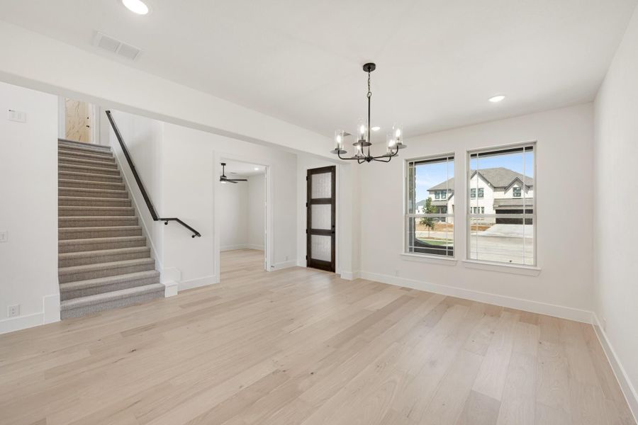 Open living area with light hardwood floors, black chandelier, carpeted staircase, and dark wood barn door.