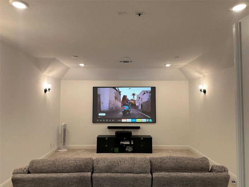 Dedicated media room featuring a large wall-mounted screen, recessed lighting, and wall sconces Dedicated media room featuring a large wall-mounted screen, recessed lighting, and wall sconces