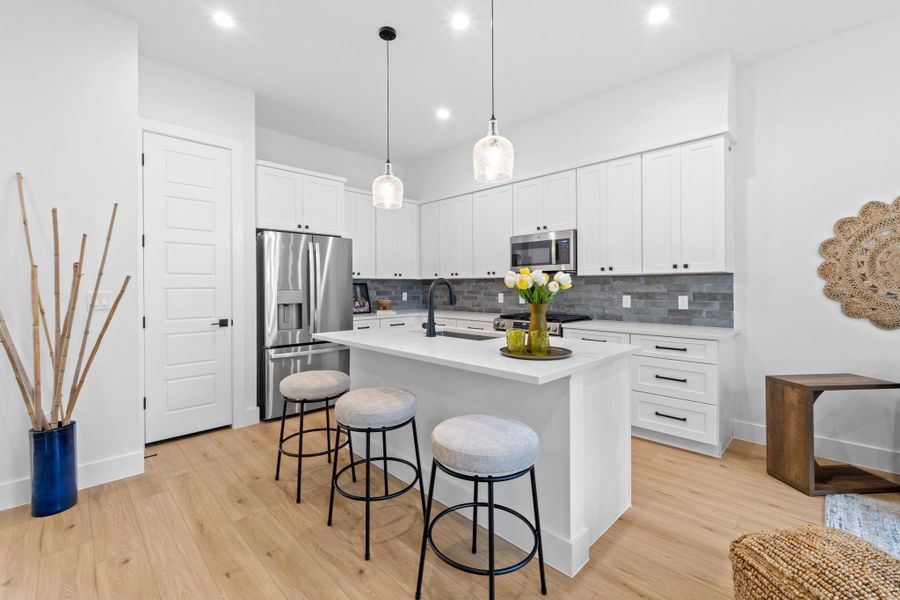 Kitchen featuring a breakfast bar, a center island with sink, stainless steel appliances, pendant lighting, and white cabinetry