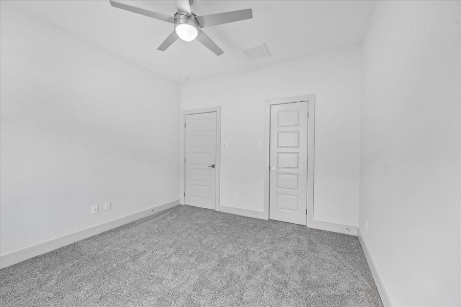This room features plush carpet, a modern ceiling fan, and two doors, providing a clean and versatile space. This room features plush carpet, a modern ceiling fan, and two doors, providing a clean and versatile space.