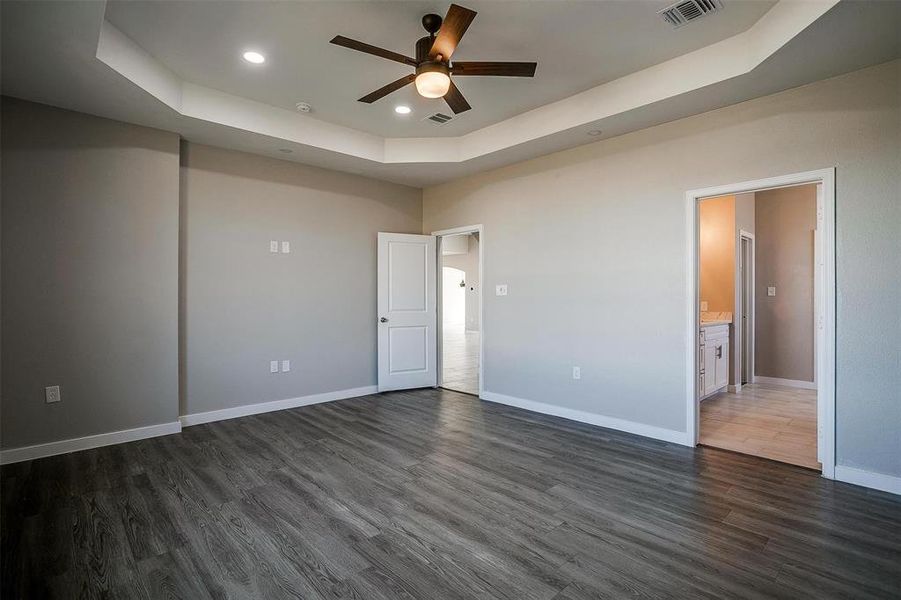 Unfurnished bedroom with dark hardwood / wood-style flooring, a tray ceiling, ceiling fan, and ensuite bathroom