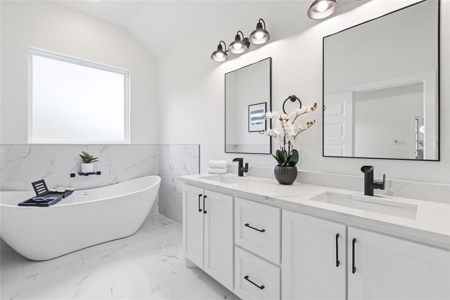 Bathroom featuring double vanity, a freestanding tub, light marble finish floors, tile walls, and a wainscoted wall