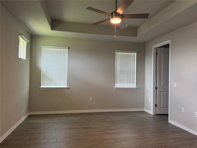 A spacious primary bedroom featuring a tray ceiling, recessed lighting, and durable wood flooring.