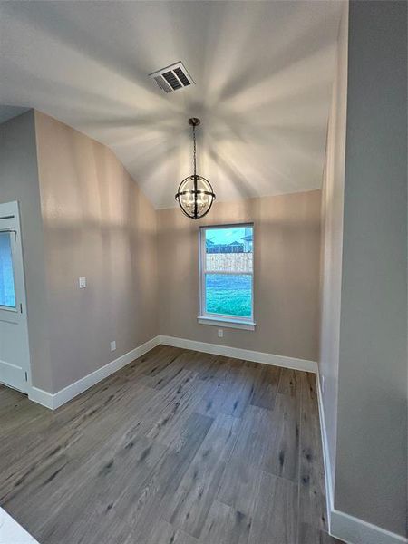 Unfurnished dining area with a notable chandelier, vaulted ceiling, and hardwood / wood-style floors