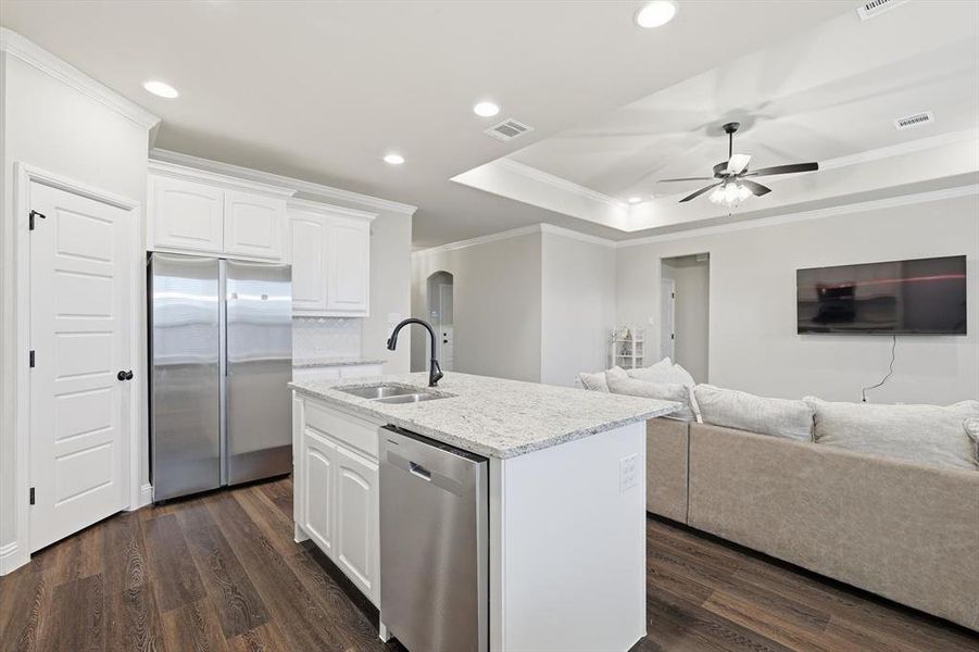 Kitchen with appliances with stainless steel finishes, white cabinets, light stone countertops, crown molding, and dark wood finished floors