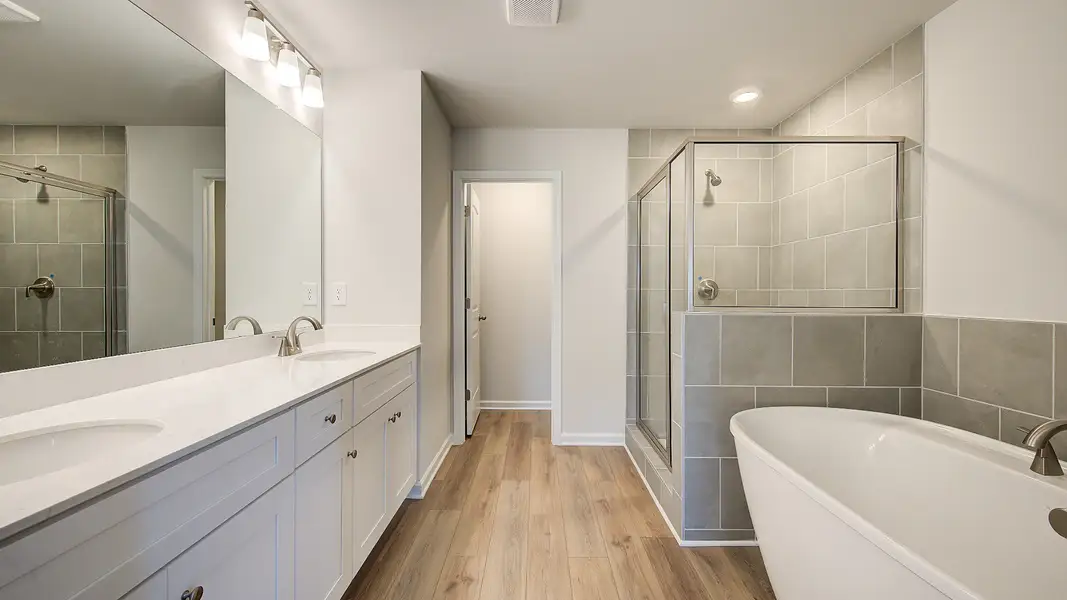 Meridian II primary bath with dual vanities and modern tile throughout floors, tub surround, and walk-in shower at Brighton.