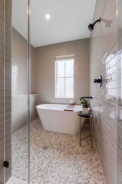 Relax in the spa-inspired primary bath featuring a freestanding soaking tub, oversized walk-in shower, floor-to-ceiling tilework, and elegant details.