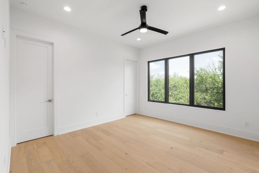 A well-lit bedroom features hardwood floors, recessed lighting, and a modern ceiling fan.