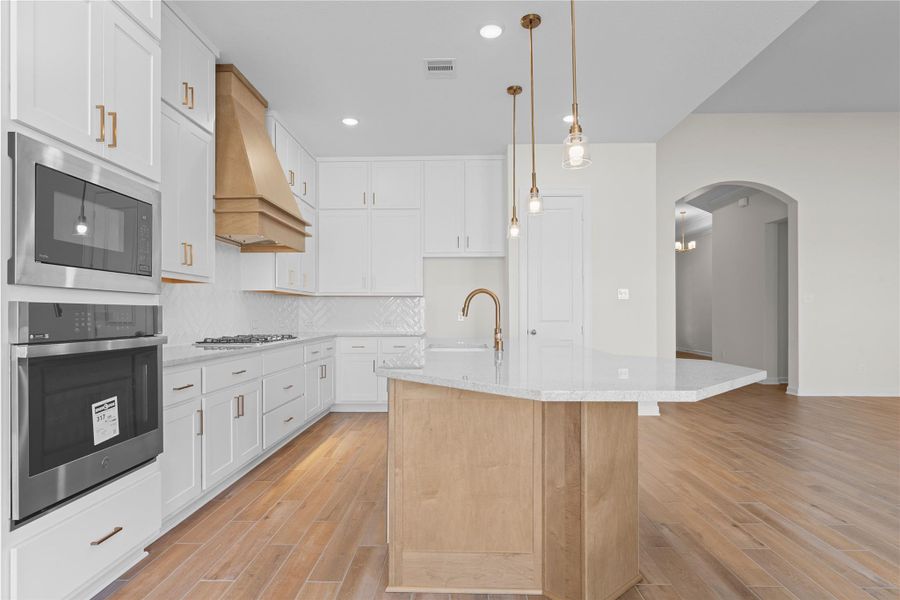 A wider perspective reveals the thoughtful layout of the kitchen, with the island serving as the heart of the space, surrounded by abundant cabinetry, quality appliances, and open sightlines that enhance the flow into the family room.