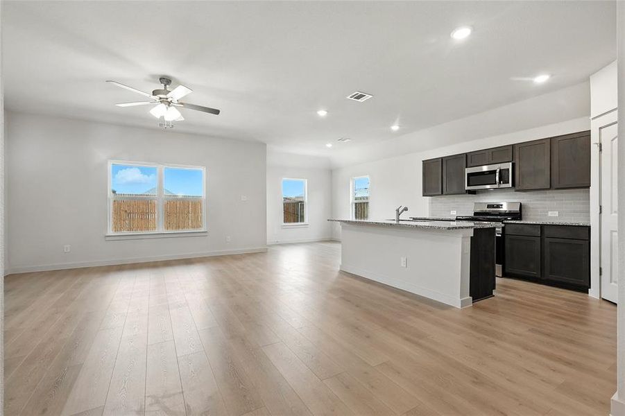 Kitchen with open floor plan, stainless steel appliances, dark wood finish cabinets, light stone countertops, and ceiling fan