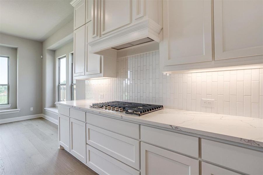 Kitchen with light stone counters, tasteful backsplash, stainless steel gas cooktop, light hardwood / wood-style flooring, and white cabinetry