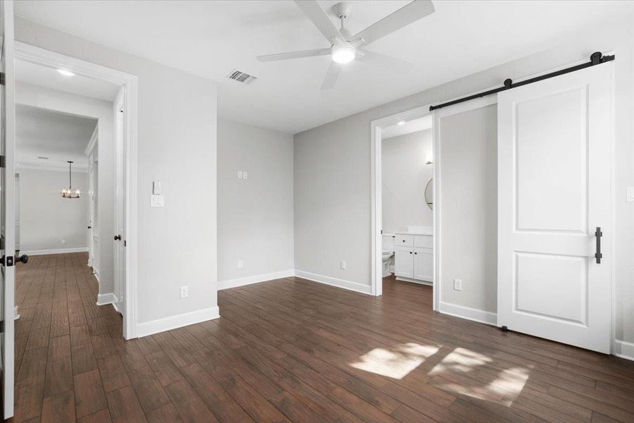 Unfurnished bedroom with a barn door, dark wood finished floors, baseboards, and ensuite bathroom Unfurnished bedroom with a barn door, dark wood finished floors, baseboards, and ensuite bathroom