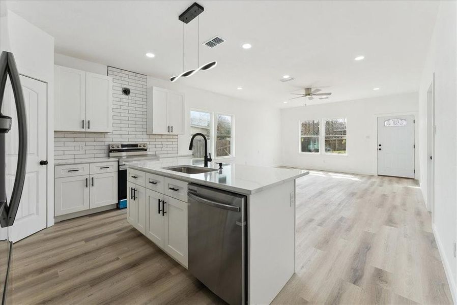 Kitchen with stainless steel appliances, visible vents, backsplash, light wood-style floors, and a sink