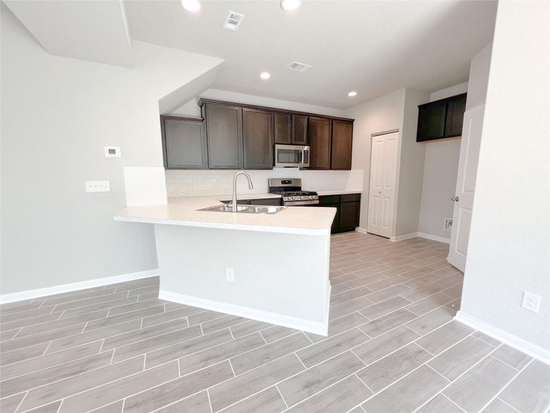 Kitchen with a peninsula, stainless steel appliances, recessed lighting, backsplash, and wood tiled floors
