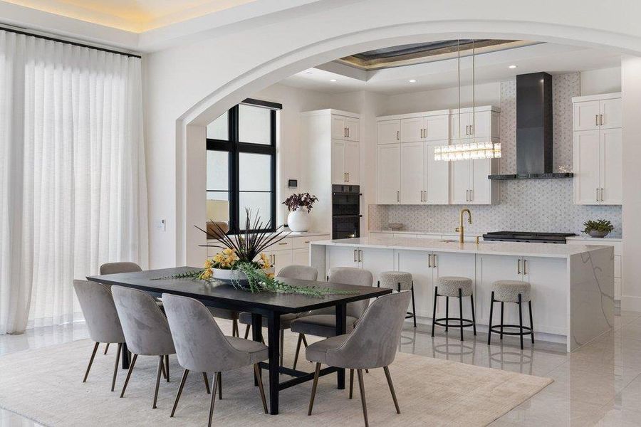 An open concept kitchen and dining area features an elegant black dining table, light gray chairs, and a spacious kitchen island with bar stool seating.